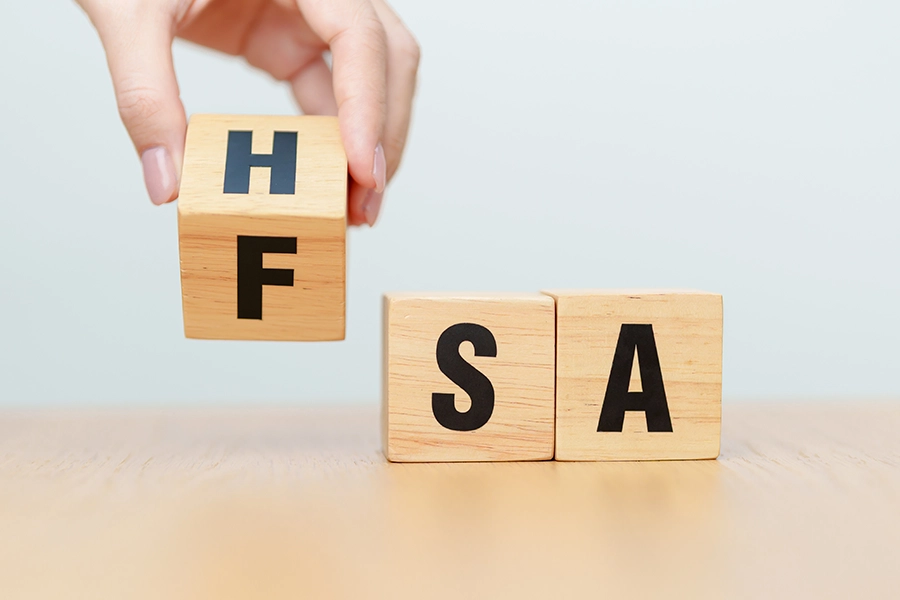 A hand turns a wooden block from F to H beside blocks spelling S and A, changing FSA to HSA.